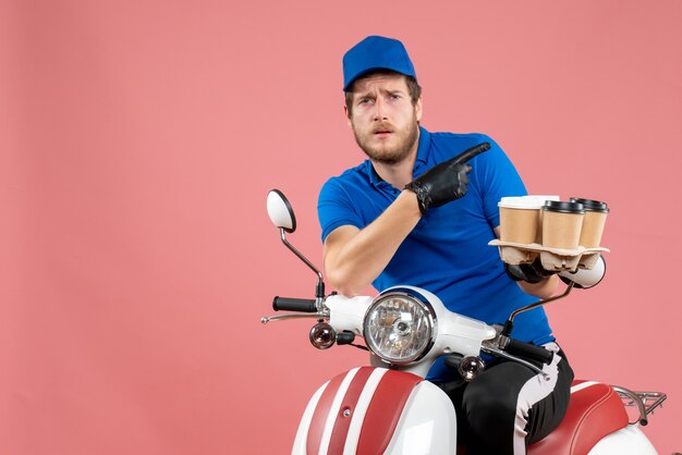 Coursier mâle vue de face assis sur un vélo et tenant des tasses à café sur le rose