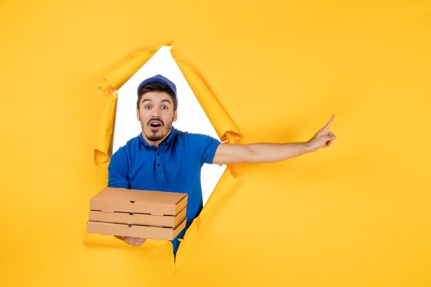 Coursier mâle vue de face tenant des boîtes à pizza sur un espace jaune clair