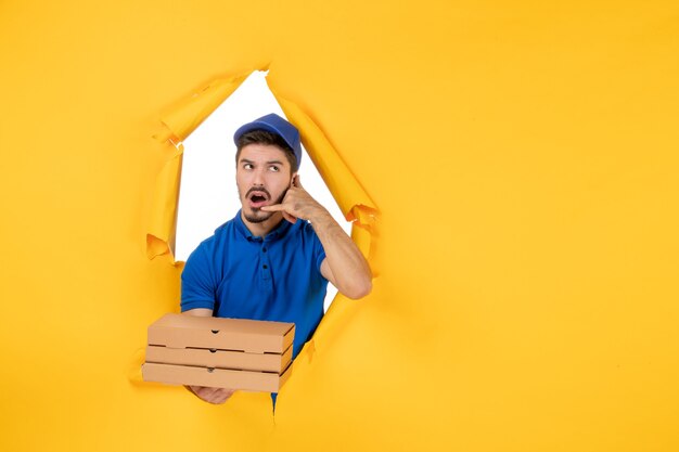 Coursier mâle vue de face tenant des boîtes à pizza sur un espace jaune