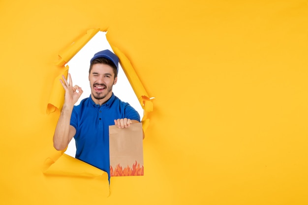 Photo gratuite coursier mâle vue de face en uniforme bleu avec emballage alimentaire sur espace jaune