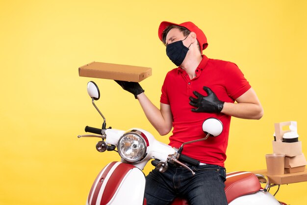 Coursier mâle vue de face à vélo en masque avec boîte de nourriture sur jaune