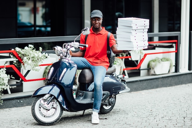 Photo gratuite un coursier masculin transporte de lourdes boîtes de colis conduit lentement sur une moto porte un casque de protection sur la tête