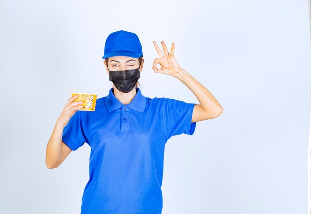 Coursière du restaurant en uniforme bleu et masque facial livrant un plat à emporter et garantissant le bon goût.