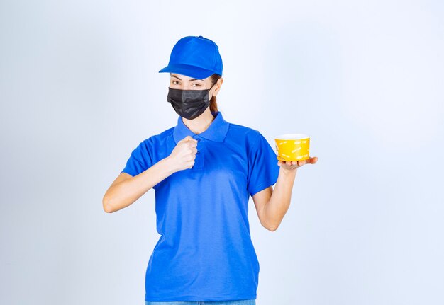 Coursière du restaurant en uniforme bleu et masque facial livrant un plat à emporter et garantissant le bon goût.