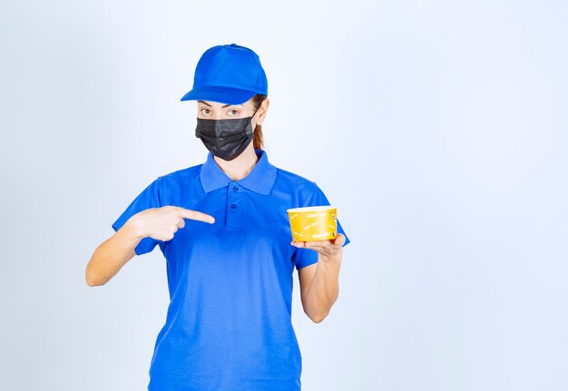 Coursière du restaurant en uniforme bleu et masque facial tenant un plat à emporter.