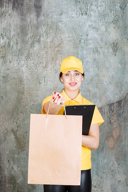 Photo gratuite coursière portant un uniforme jaune livrant un sac en carton et tenant un dossier noir.