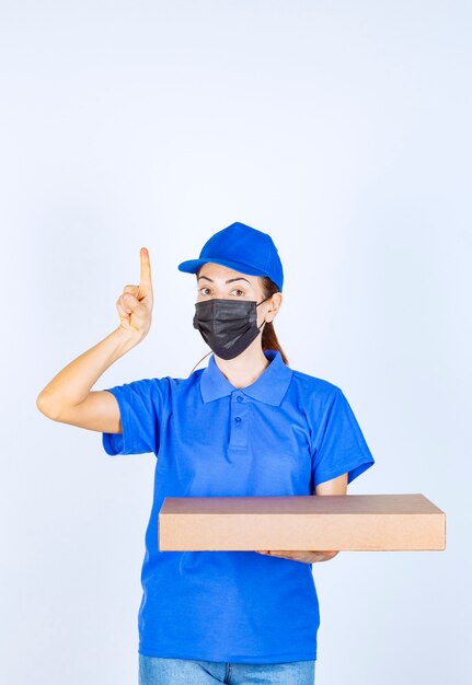 Coursière en uniforme bleu et masque facial tenant une boîte en carton et pointant quelque part.