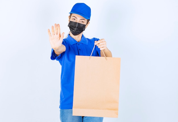 Coursière en uniforme bleu et masque facial tenant un sac en carton et refusant de prendre autre chose.