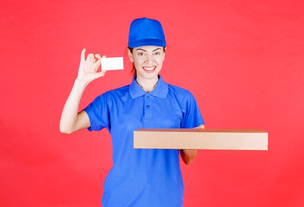 Coursière en uniforme bleu tenant une boîte en carton et présentant sa carte de visite.