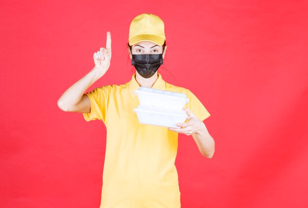 Coursière en uniforme jaune et masque noir tenant plusieurs colis à emporter et ayant une bonne idée