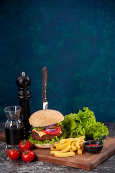 Couteau en sandwich à la viande et tomates frites avec paquet vert tige sur planche de bois sauce ketchup sur surface bleu foncé