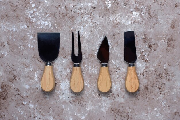 Couteaux à fromage avec manches en bois, fourchette, spatule sur surface marron clair.
