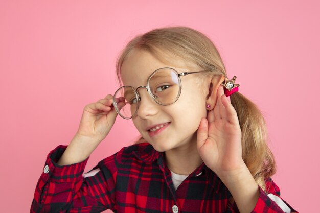 Écoutez les secrets. Portrait de petite fille caucasienne sur mur rose. Beau modèle féminin aux cheveux blonds.