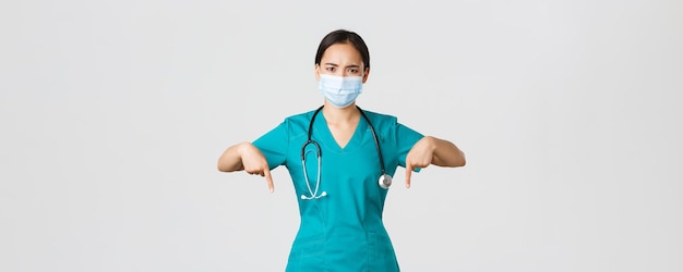 Covid-19, maladie à coronavirus, concept des travailleurs de la santé. une femme médecin asiatique inquiète à l'air sérieux informe les patients, le médecin portant un masque médical et des gommages fronçant les sourcils, pointant les doigts vers le bas