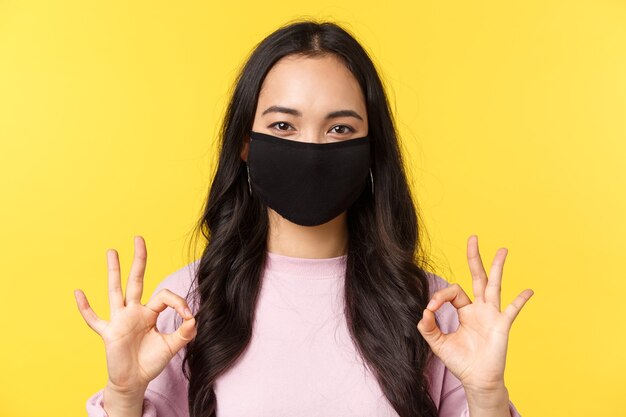 Covid-19, mode de vie de distanciation sociale, empêche le concept de propagation du virus. Gros plan d'une femme asiatique souriante et heureuse en masque facial, prenez tout sous contrôle, montrez une bonne connexion, aimez et recommandez.