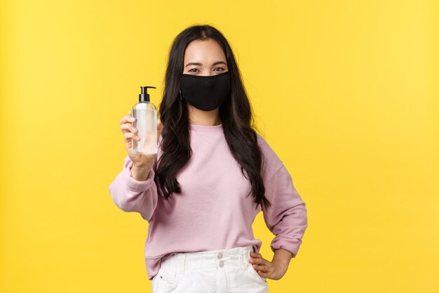Covid-19, mode de vie de distanciation sociale, empêche le concept de propagation du virus. Joyeuse fille asiatique en masque facial utilisant toujours un désinfectant pour les mains pendant la pandémie de coronavirus, recommande un produit d'hygiène.