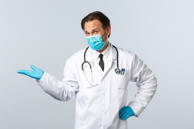 Covid-19, prévention du virus, travailleurs de la santé et concept de vaccination. Un médecin sceptique portant un masque médical et des gants pointant vers la gauche et regardant la caméra mécontent, donne un avis négatif