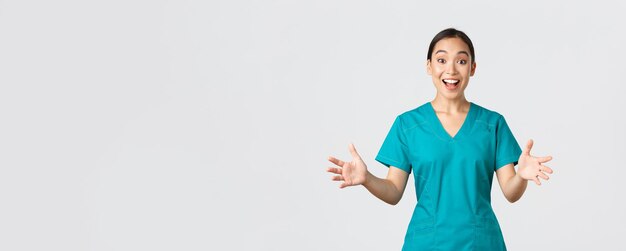 Covid-19, travailleurs de la santé, concept de pandémie. Infirmière asiatique heureuse et surprise en gommage levant les mains excitée et souriante. Le docteur félicite avec de bonnes nouvelles, des applaudissements, un fond blanc.