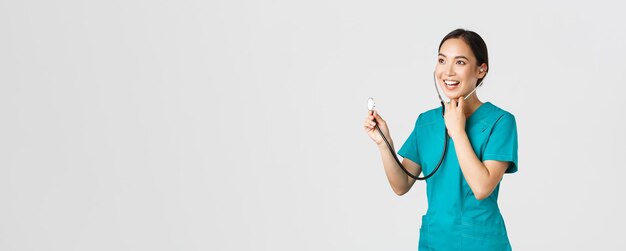 Covid-19, travailleurs de la santé et prévention du concept de virus. Femme médecin asiatique souriante et amicale écoutant les poumons du patient pendant l'examen quotidien, à l'aide d'un stéthoscope, fond blanc