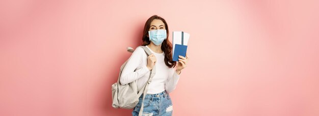 Covid et concept de voyage femme heureuse voyageuse en masque médical détenant un passeport et un tic d'avion