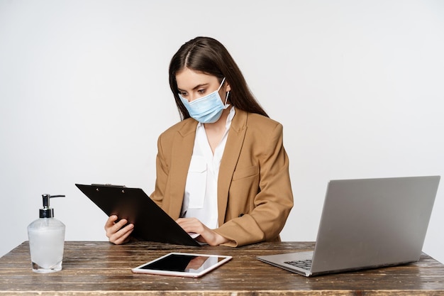 Covid, pandémie et concept de lieu de travail de bureau. Portrait d'une femme d'entreprise portant un masque médical contre le coronavirus, travaillant, debout sur fond blanc.