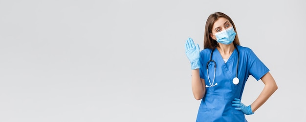 Covid19 empêchant le virus de la santé des travailleurs de la santé et le concept de quarantaine Infirmière amicale en clinique portant des gommages bleus et un masque médical agitant le signe bonjour ou salut avec des gants