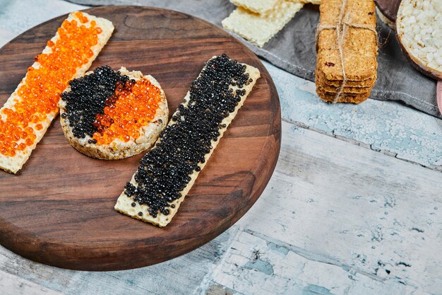 Craquelins de riz au caviar rouge et noir sur plaque de bois.