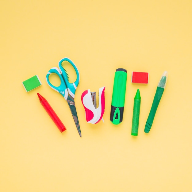 Des crayons; ciseaux; surligneur; agrafeuse et gomme disposées sur une surface jaune