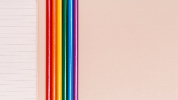 Crayons colorés arc-en-ciel et cahier sur fond beige