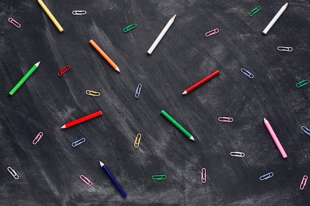 Crayons colorés et trombones sur tableau noir
