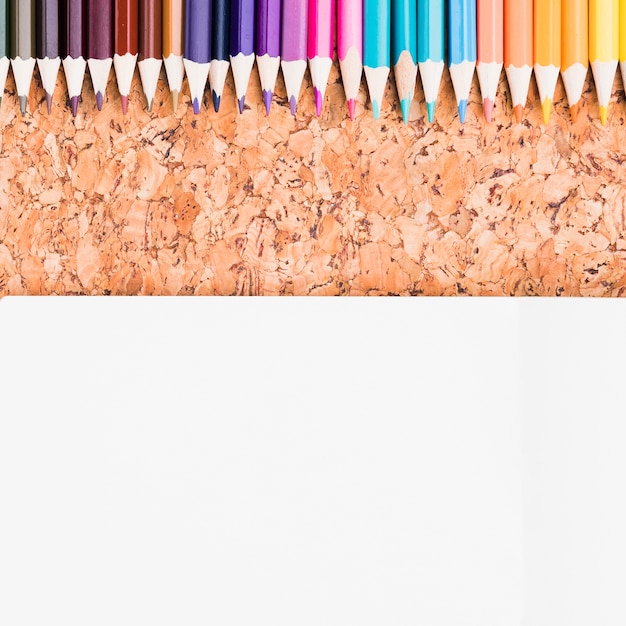 Crayons de couleur placés au-dessus d&#39;une feuille de papier sur un fond de liège