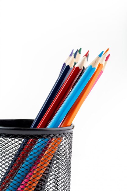 Crayons multicolores pour la peinture et le dessin à l'intérieur d'un petit panier noir sur mur blanc