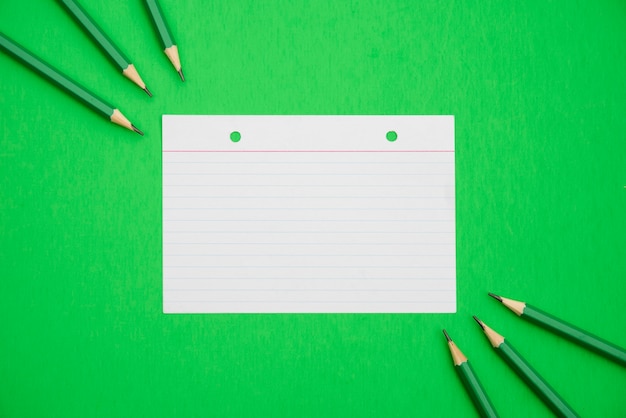 Crayons pointus et papier à lignes texturé sur fond vert clair