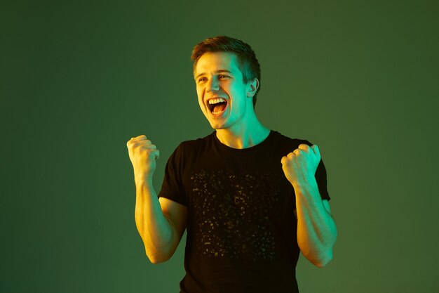 Crazy happe, célèbre la victoire. Portrait de l'homme caucasien isolé sur fond de studio vert en néon.