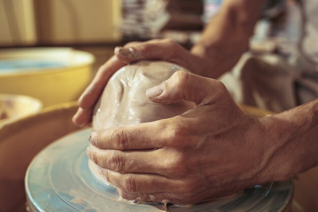 Création d'un pot ou d'un vase d'argile blanche en gros plan. Maître pot. Mains d'homme faisant macro de cruche d'argile. Le sculpteur dans l'atelier fabrique une cruche en gros plan en faïence. Tour de potier tordu.