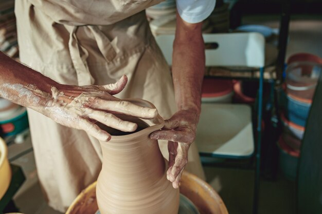 Création d'un pot ou d'un vase d'argile blanche en gros plan. Maître pot. Mains d'homme faisant macro de cruche d'argile. Le sculpteur dans l'atelier fabrique une cruche en gros plan en faïence. Tour de potier tordu.