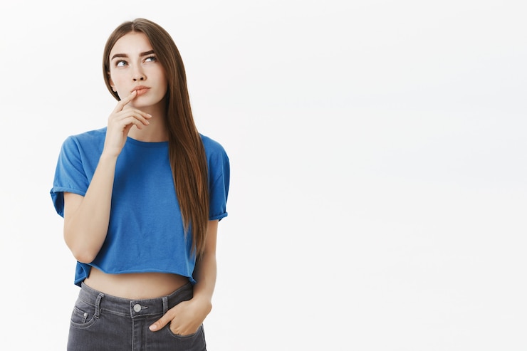 Photo gratuit créative intelligente et réfléchie jolie femme européenne en haut court bleu à la mode faisant un geste hmm avec le doigt sur la lèvre inférieure en levant le sourcil et en regardant, pensant faire un choix à l'esprit