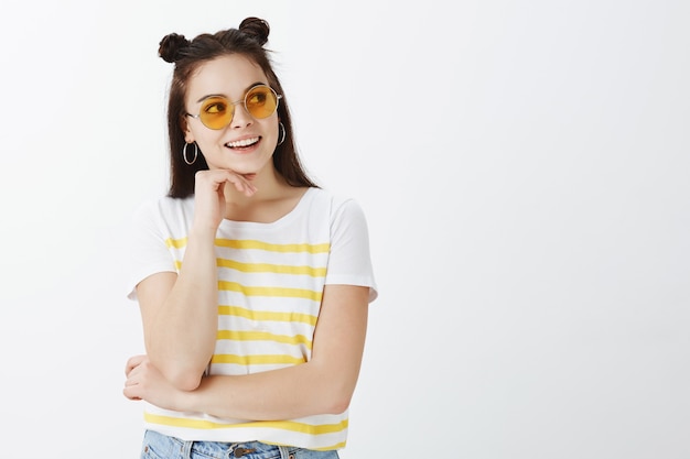 Créative jeune femme posant avec des lunettes de soleil contre le mur blanc