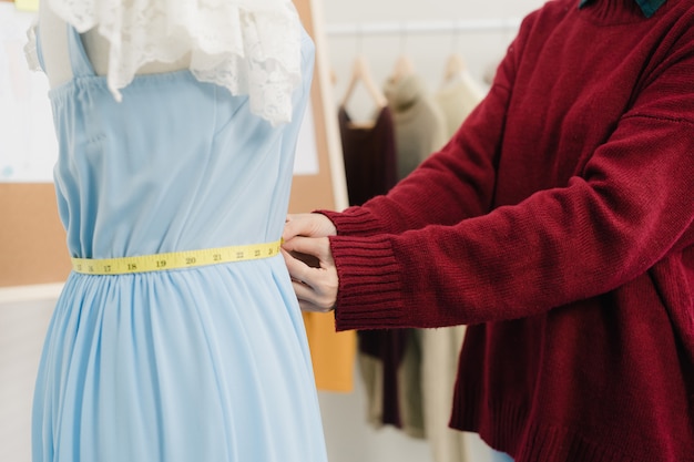 Créatrice de mode professionnelle belle asiatique travaillant la robe de mesure sur un vêtement mannequin