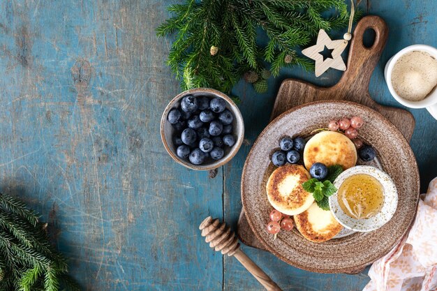 Crêpes au fromage cottage Gâteaux au fromage avec des groseilles au miel et des myrtilles sur fond bleu Aliments sucrés pour le petit-déjeuner pour le Nouvel An