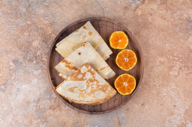 Crêpes au lait servies avec des tranches d'orange dans un plateau en bois