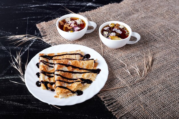 Crêpes dans une assiette blanche avec du sirop de chocolat et du thé.