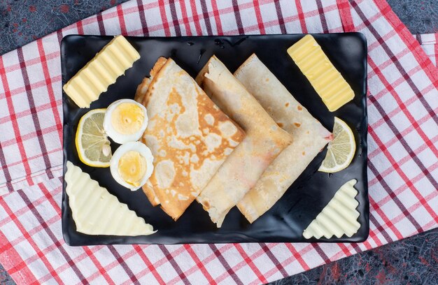 Crêpes avec oeuf, fromage et beurre sur un plateau.