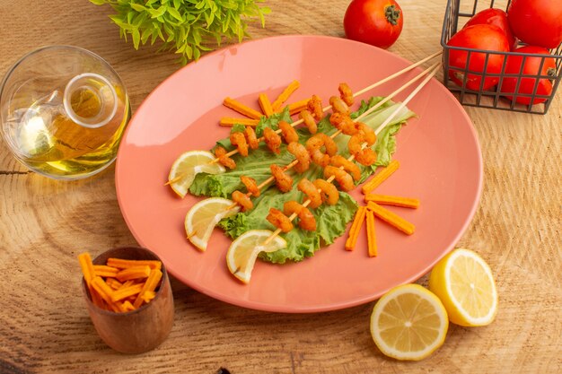 Crevettes cuites sur des bâtons à l'intérieur de la plaque de pêche avec des tranches de citron huile de salade verte sur un bureau en bois