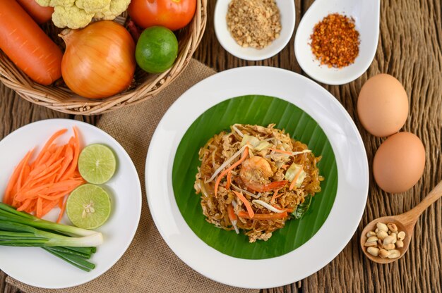 Crevettes Padthai dans un bol noir avec des œufs, de l'oignon de printemps et de l'assaisonnement sur une table en bois.