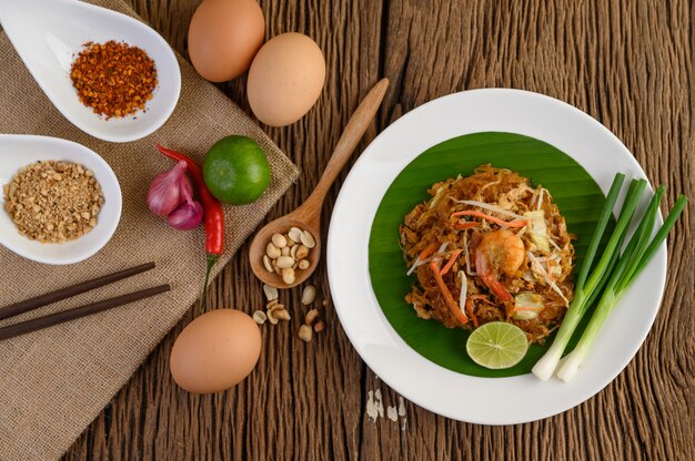 Crevettes Padthai dans un bol noir avec des œufs, de l'oignon de printemps et de l'assaisonnement sur une table en bois.