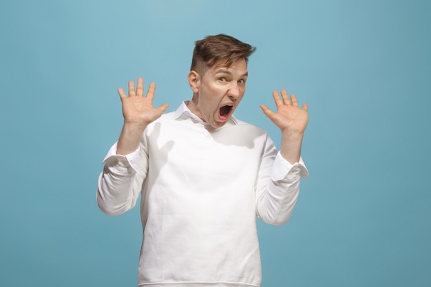 Crier, haine, rage. Pleurer un homme en colère émotionnel criant sur fond bleu de studio. Visage jeune et émotionnel. portrait de demi-longueur masculine. Émotions humaines, concept d'expression faciale. Couleurs tendance