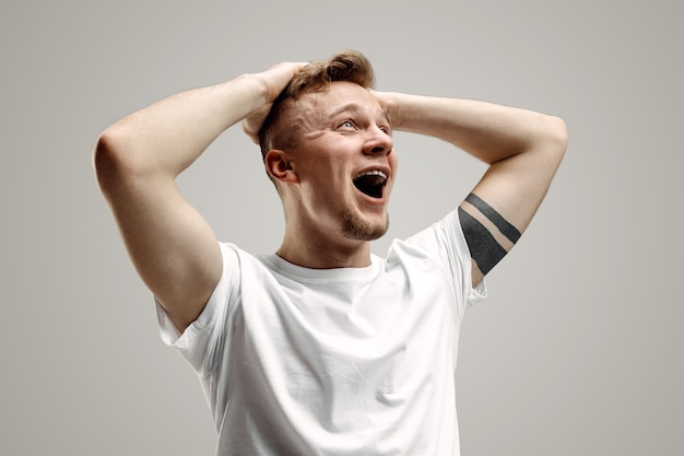 Photo gratuite crier, haine, rage. pleurer un homme en colère émotionnel criant sur fond gris de studio. visage jeune et émotionnel. portrait de demi-longueur masculine. émotions humaines, concept d'expression faciale.