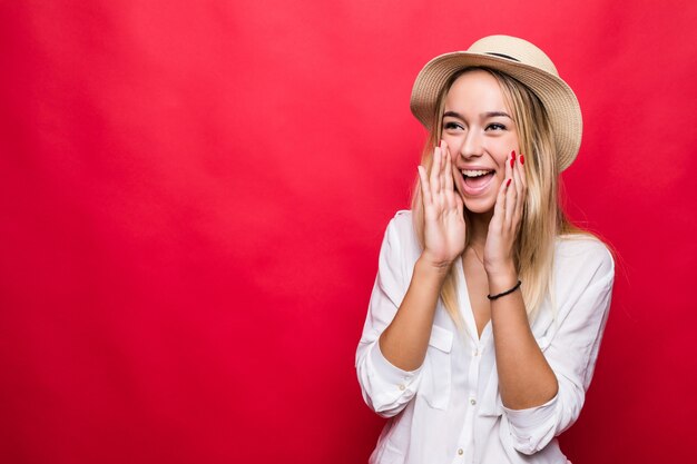 Crier jeune femme au chapeau de paille debout isolé sur mur rouge.