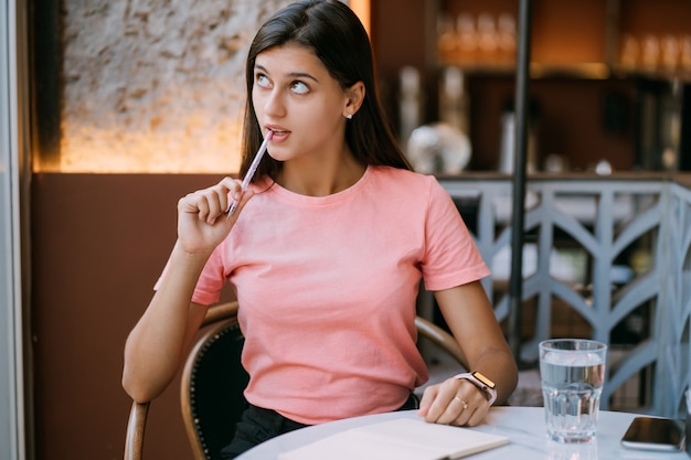 Écriture de produits laitiers en note dans un café, concept comme mémoire de la vie. Femme au café. Femme souriante faisant des notes bloc-notes.